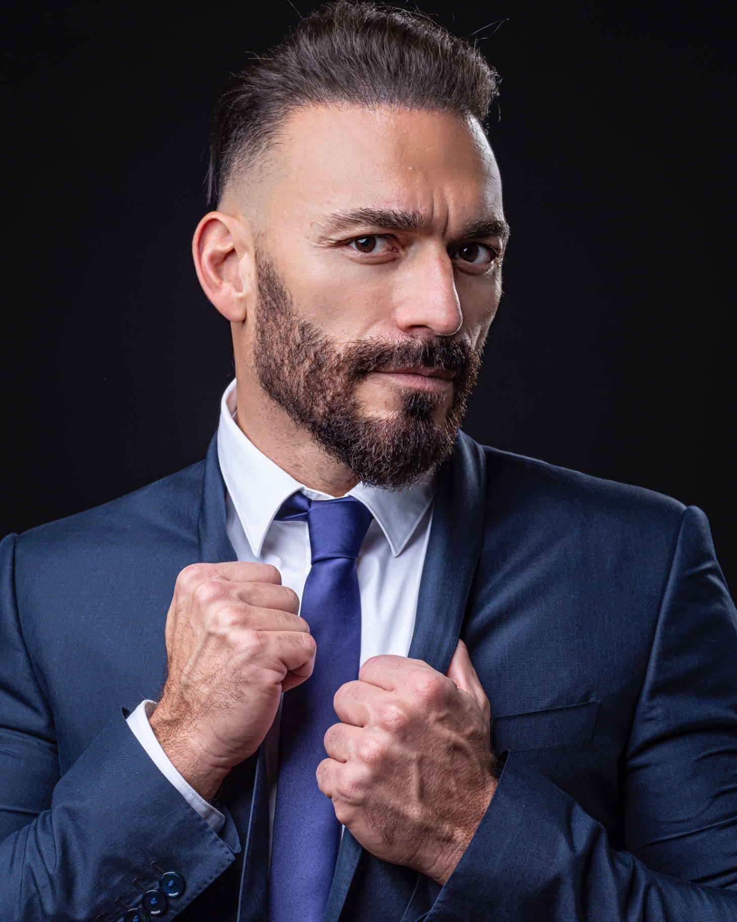 Dark studio portrait of Gianluca Margheri adjusting his blue tie